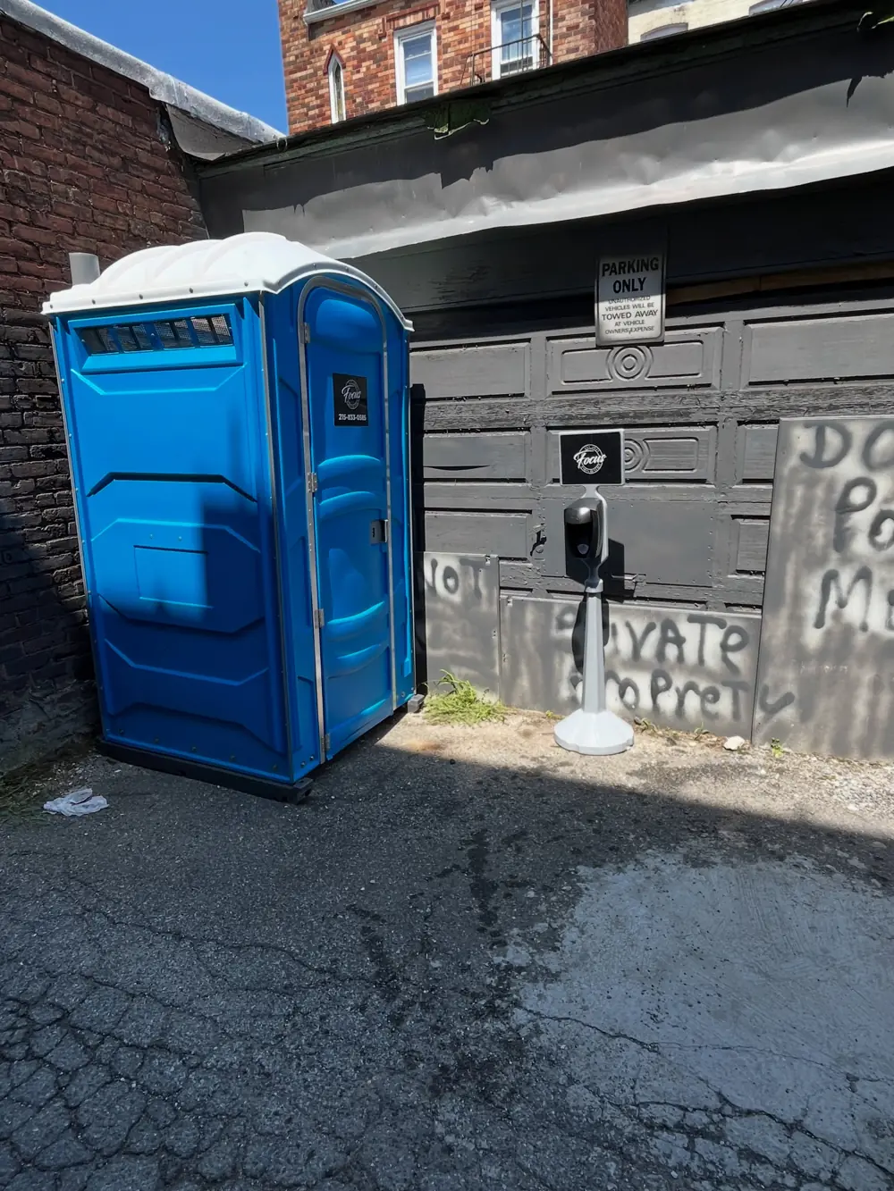 Blue porta potty placed in a narrow alley beside a job site wall