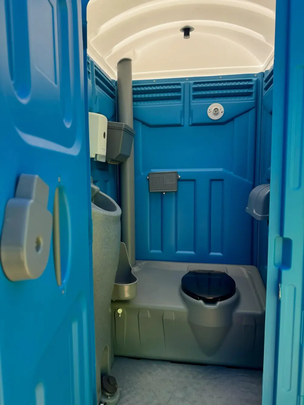 Inside a blue standard porta potty showing urinal and toilet seat