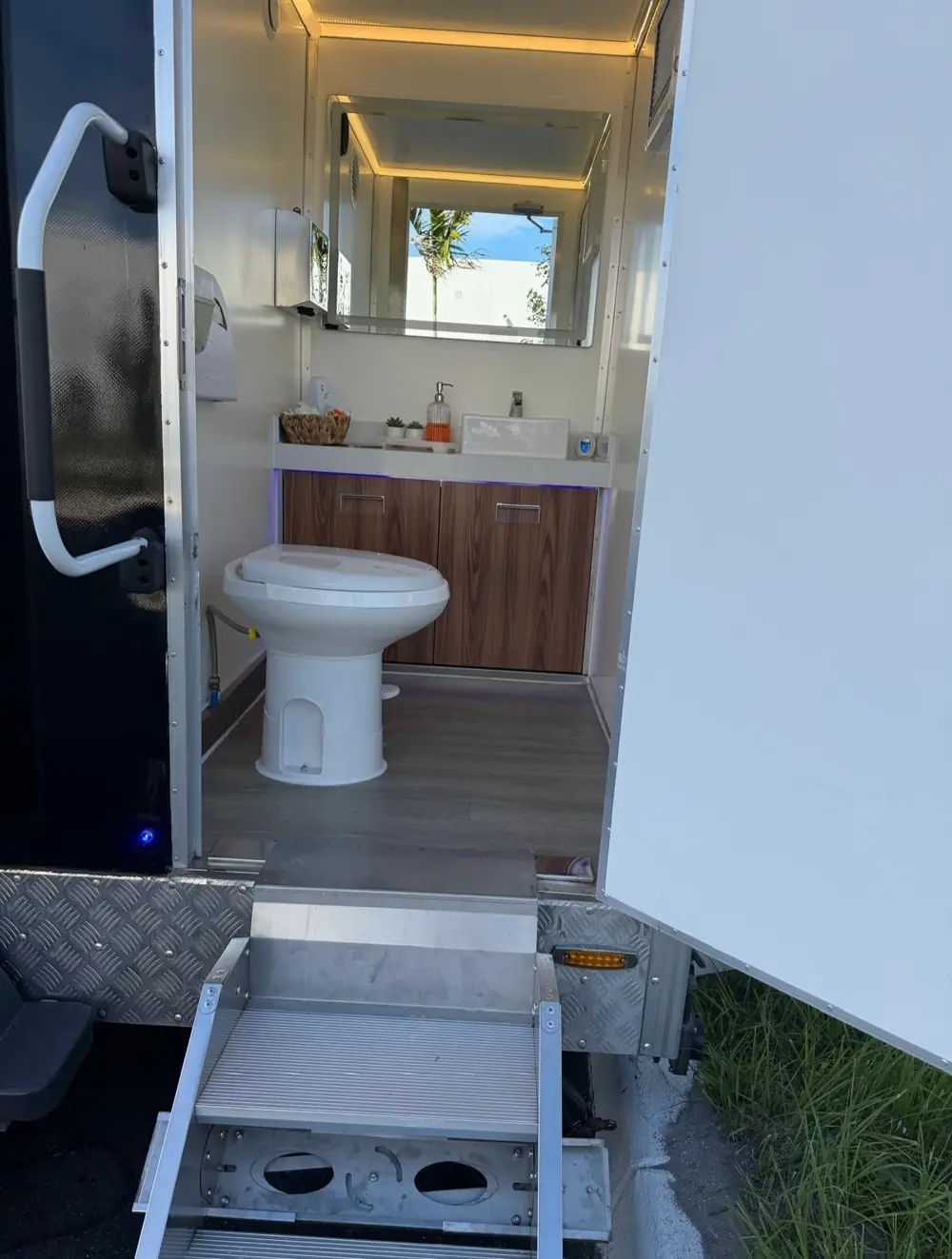 Restroom trailer door open showing toilet and lit interior above metal steps